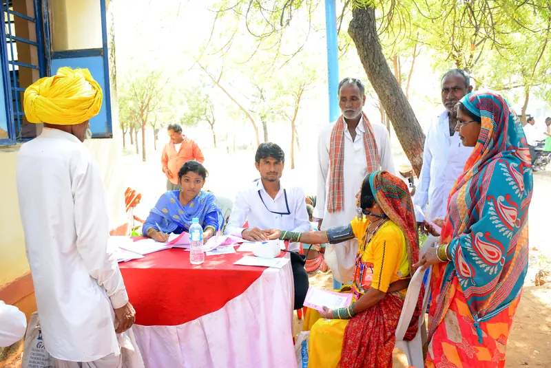 The screening team at a table under a tree, with villagers gathered around